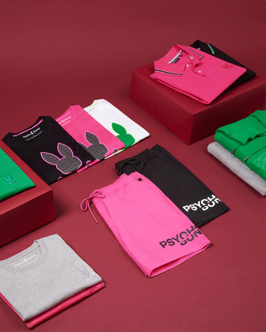 folded neon clothes in pink, green, black, gray and black from psycho bunny on a burgundy background